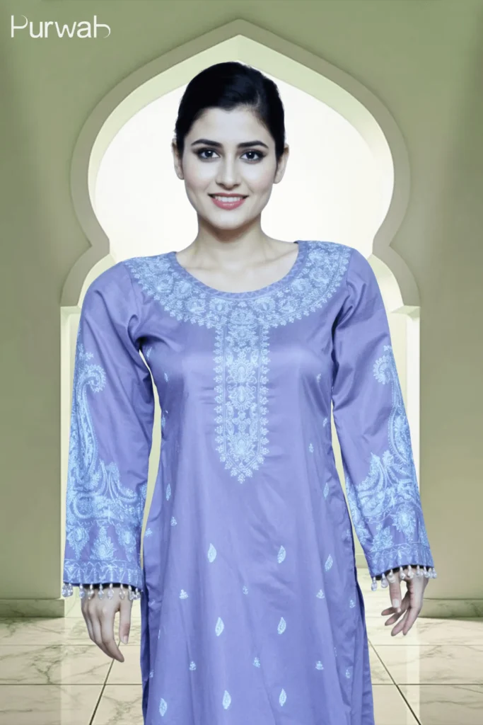 A woman wearing a purple embroidered kurta with long sleeves, posing against a traditional arched background. The design features intricate blue patterns on the front and sleeves.