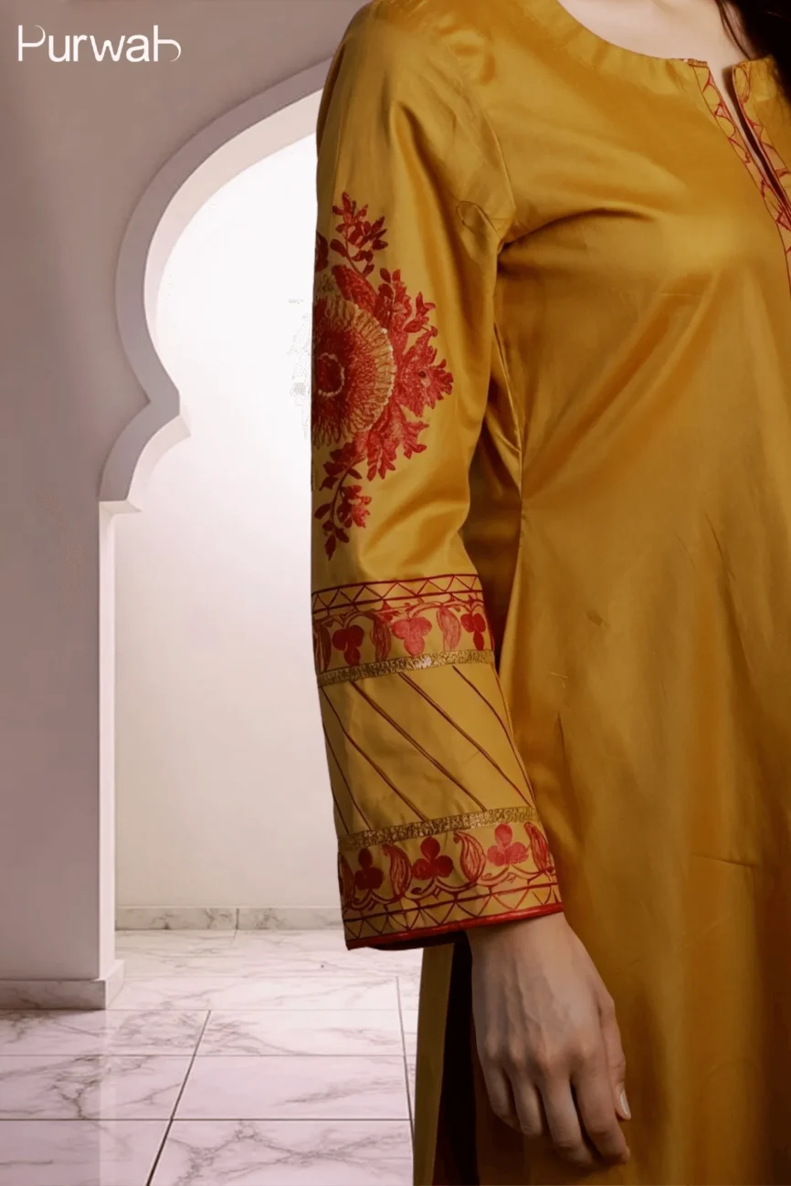 Close-up shot of a mustard-colored embroidered shirt sleeve with floral designs and intricate detailing on the cuff.